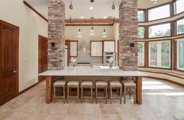 kitchen with stainless steel appliances, ornate columns, plenty of natural light, and wall chimney exhaust hood