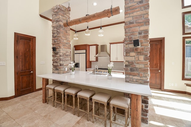 kitchen with wall chimney range hood, a kitchen bar, decorative columns, and a towering ceiling