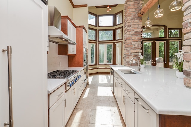 kitchen featuring a wealth of natural light, decorative light fixtures, wall chimney range hood, and sink