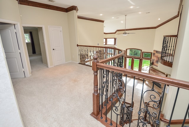 corridor featuring a high ceiling, plenty of natural light, crown molding, and light colored carpet