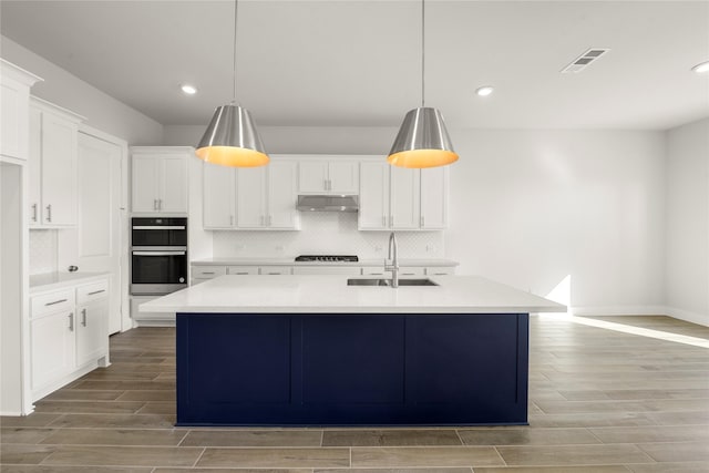 kitchen featuring stainless steel double oven, an island with sink, white cabinets, black gas cooktop, and sink