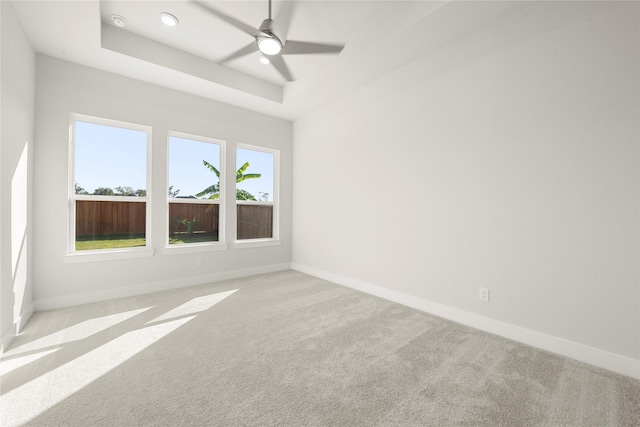 carpeted empty room with ceiling fan and a tray ceiling