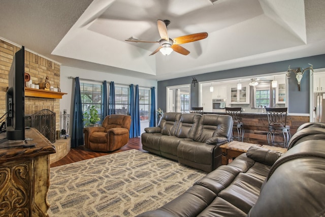 living room with a textured ceiling, a fireplace, hardwood / wood-style floors, a tray ceiling, and ceiling fan