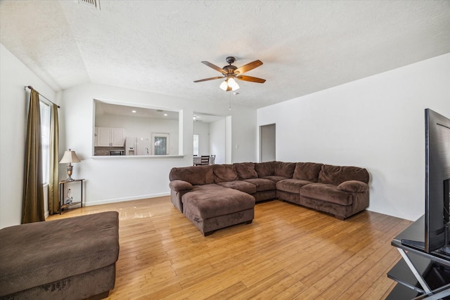 living room featuring lofted ceiling, ceiling fan, a textured ceiling, and light wood-type flooring