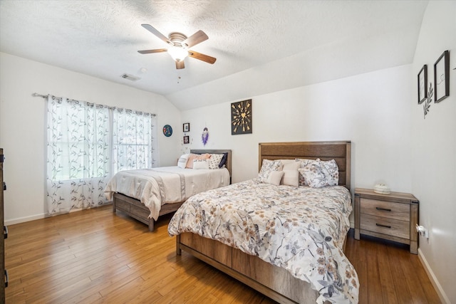 bedroom with vaulted ceiling, ceiling fan, hardwood / wood-style floors, and a textured ceiling