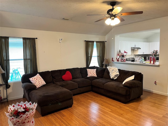 living room with ceiling fan, lofted ceiling, light hardwood / wood-style floors, and a textured ceiling