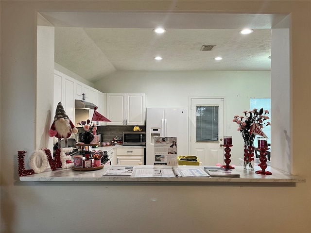 kitchen with white cabinetry, decorative backsplash, white refrigerator with ice dispenser, kitchen peninsula, and a textured ceiling