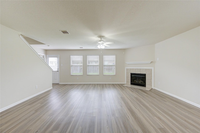 unfurnished living room featuring light wood-type flooring, a fireplace, a textured ceiling, and ceiling fan