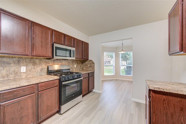 kitchen with appliances with stainless steel finishes, hanging light fixtures, a textured ceiling, decorative backsplash, and light hardwood / wood-style floors