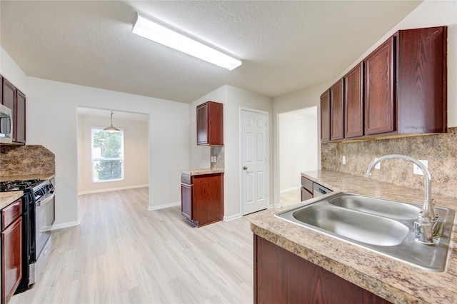 kitchen with light wood-type flooring, hanging light fixtures, range with gas stovetop, sink, and decorative backsplash