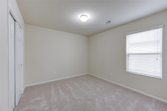 unfurnished bedroom with a closet, a textured ceiling, and light colored carpet