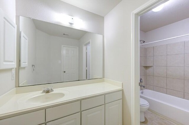 full bathroom with tiled shower / bath combo, tile patterned floors, vanity, and toilet