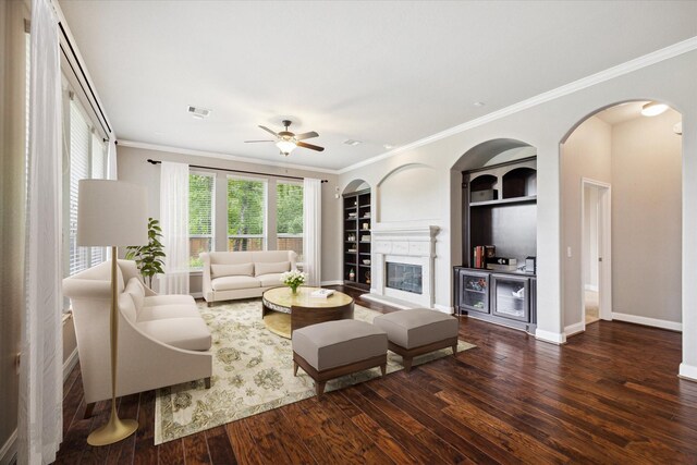 living room with hardwood / wood-style floors, built in shelves, crown molding, a fireplace, and ceiling fan