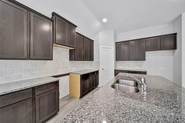 kitchen featuring lofted ceiling, light hardwood / wood-style flooring, backsplash, dark stone counters, and sink