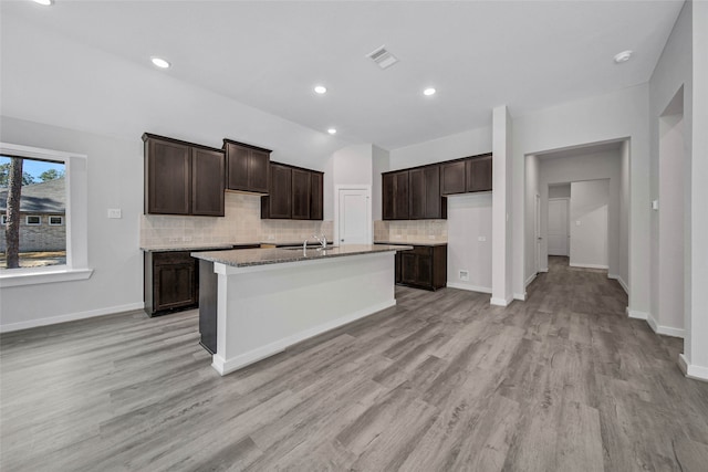 kitchen featuring dark brown cabinets, a center island with sink, sink, light hardwood / wood-style floors, and tasteful backsplash