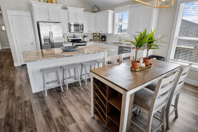 kitchen featuring stainless steel appliances, sink, light stone counters, wood-type flooring, and a center island