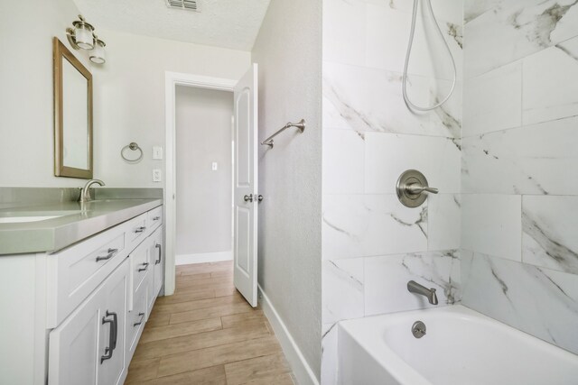 bathroom with a textured ceiling, vanity, hardwood / wood-style floors, and tiled shower / bath