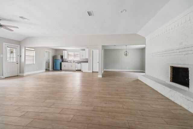 unfurnished living room featuring vaulted ceiling, sink, light wood-type flooring, a fireplace, and ceiling fan