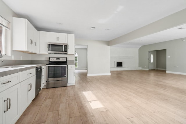 kitchen featuring white cabinets, a brick fireplace, light wood-type flooring, and stainless steel appliances