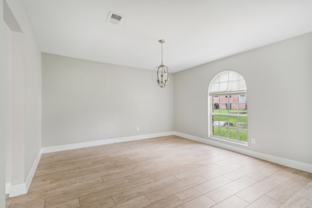 empty room with light hardwood / wood-style floors and a notable chandelier