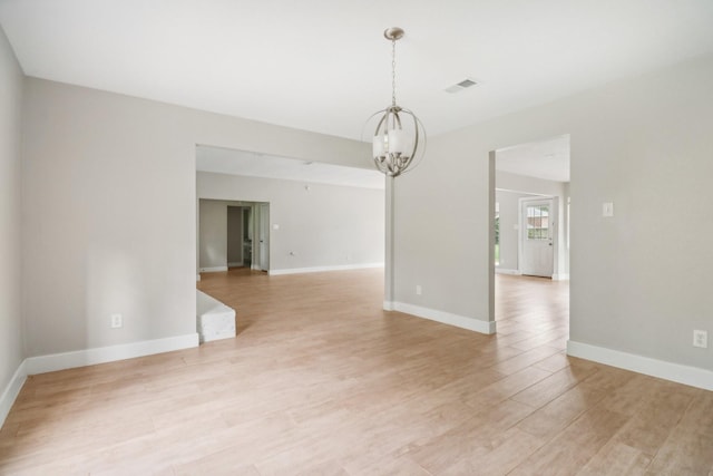 unfurnished room featuring baseboards, light wood-style flooring, visible vents, and a notable chandelier