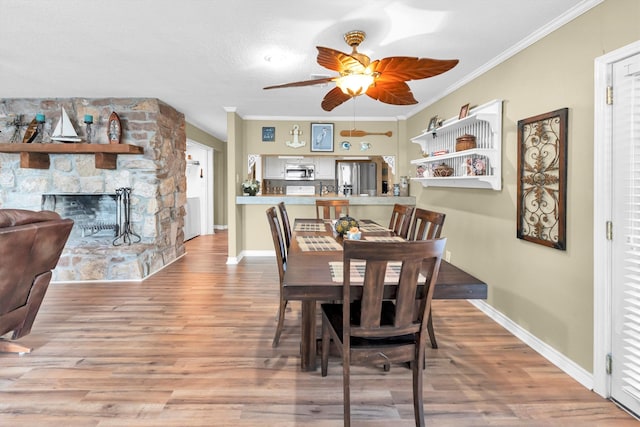 dining room featuring ceiling fan, hardwood / wood-style flooring, a fireplace, and crown molding