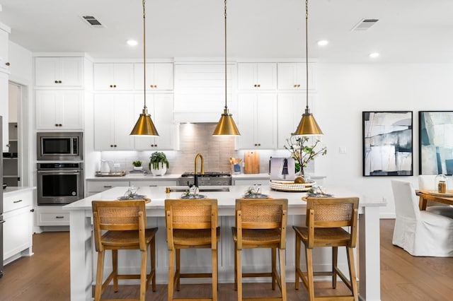 kitchen with backsplash, a kitchen island with sink, decorative light fixtures, a kitchen bar, and stainless steel appliances