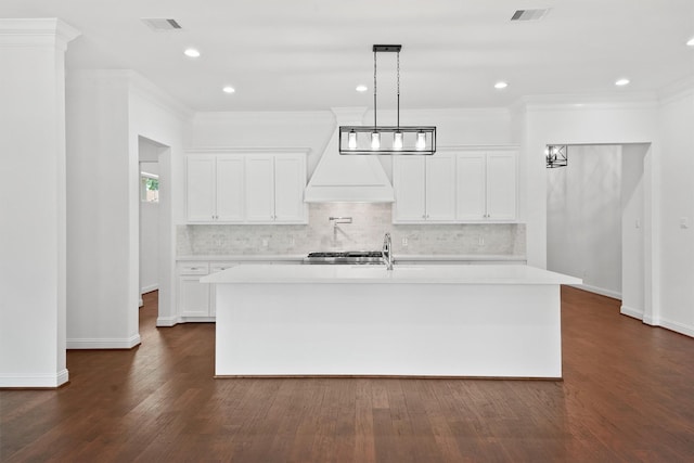 kitchen featuring dark wood-type flooring, light countertops, ornamental molding, tasteful backsplash, and a center island with sink