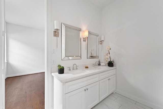 bathroom featuring double vanity, wood finished floors, a sink, and baseboards