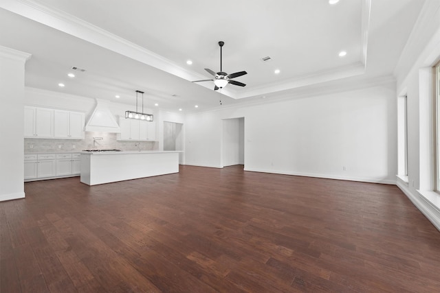 unfurnished living room featuring a raised ceiling, dark wood-style floors, ceiling fan, crown molding, and recessed lighting