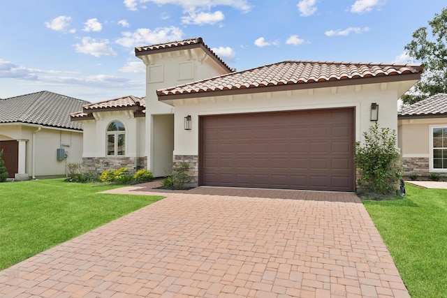 mediterranean / spanish-style house featuring an attached garage, stone siding, decorative driveway, stucco siding, and a front lawn