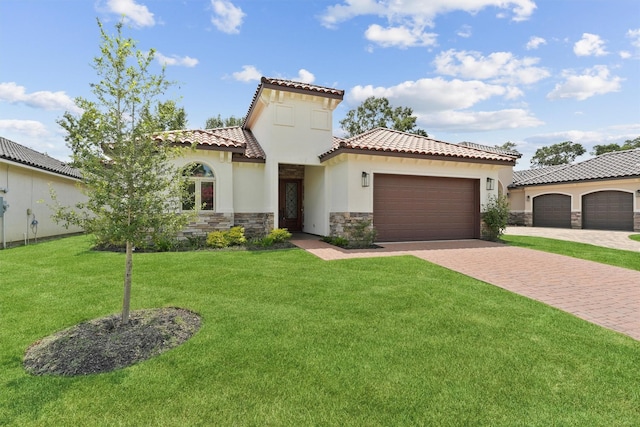 mediterranean / spanish-style home with an attached garage, stone siding, decorative driveway, stucco siding, and a front lawn