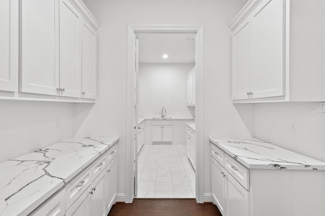 kitchen with light stone countertops, marble finish floor, white cabinetry, a sink, and recessed lighting