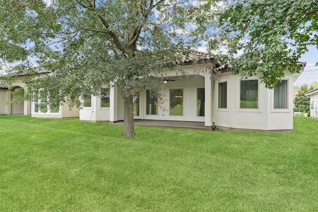 rear view of house featuring stucco siding, ceiling fan, and a yard