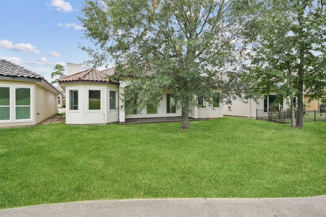 back of house with a yard, fence, stucco siding, and a tiled roof