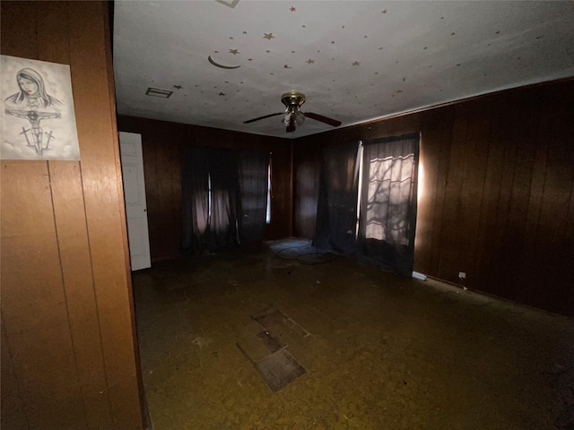 empty room with wooden walls, visible vents, and a ceiling fan