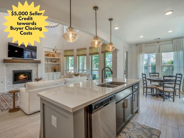 kitchen featuring decorative light fixtures, sink, built in features, stainless steel dishwasher, and a center island with sink