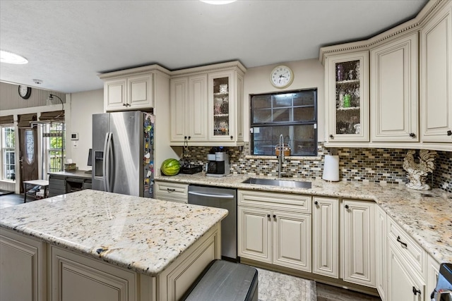 kitchen with backsplash, light stone counters, stainless steel appliances, sink, and cream cabinetry