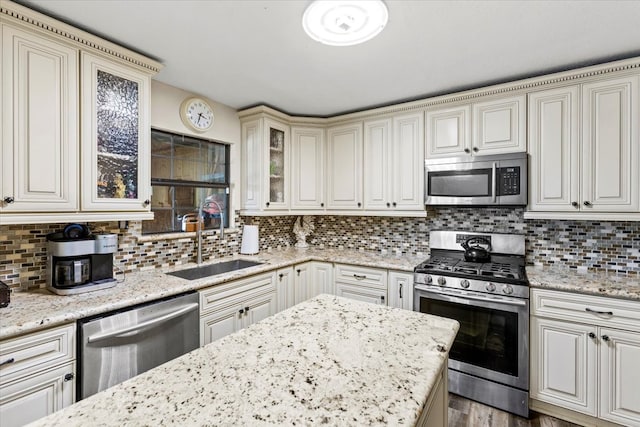 kitchen with tasteful backsplash, light stone counters, sink, appliances with stainless steel finishes, and hardwood / wood-style flooring