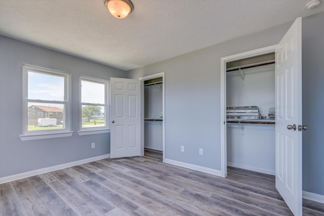 unfurnished bedroom featuring wood finished floors, baseboards, multiple closets, and a textured ceiling