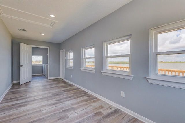 unfurnished room featuring light wood-type flooring, visible vents, baseboards, and attic access