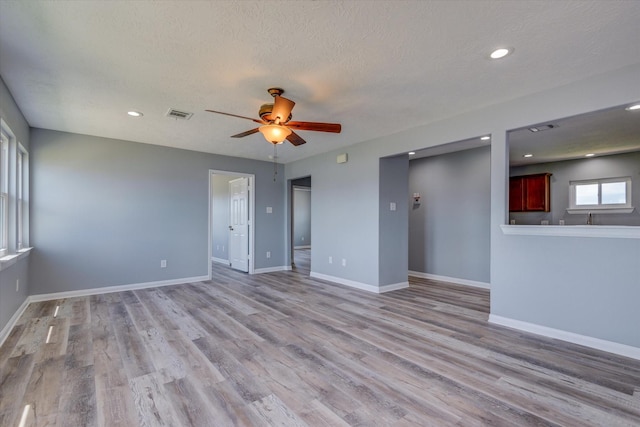 empty room featuring light wood finished floors, visible vents, ceiling fan, baseboards, and a textured ceiling