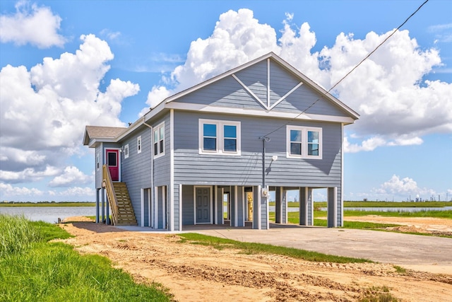 back of property featuring stairway, a water view, a carport, and driveway