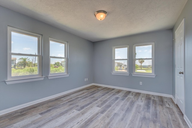 spare room featuring baseboards, light wood finished floors, and a textured ceiling