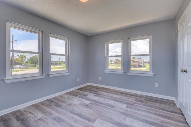 unfurnished room with a textured ceiling, baseboards, and wood finished floors