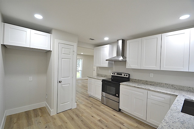 kitchen with wall chimney range hood, stainless steel electric stove, white cabinetry, light hardwood / wood-style floors, and light stone counters