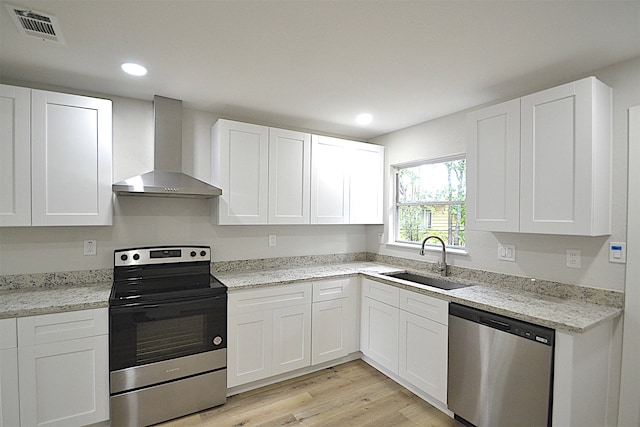 kitchen with wall chimney range hood, white cabinetry, light hardwood / wood-style floors, sink, and stainless steel appliances