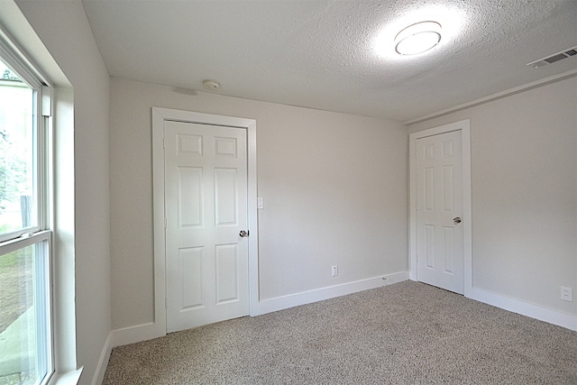 unfurnished bedroom featuring carpet flooring, a textured ceiling, and multiple windows