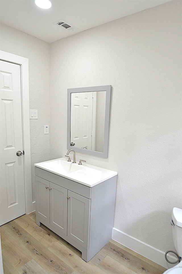 bathroom with toilet, vanity, and wood-type flooring