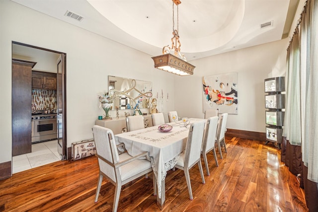 dining space with a raised ceiling and light wood-type flooring